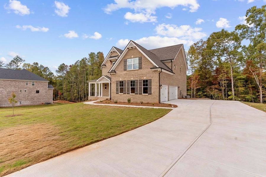 Two-story brick house with a driveway, garage, and lawn under a partly cloudy sky.