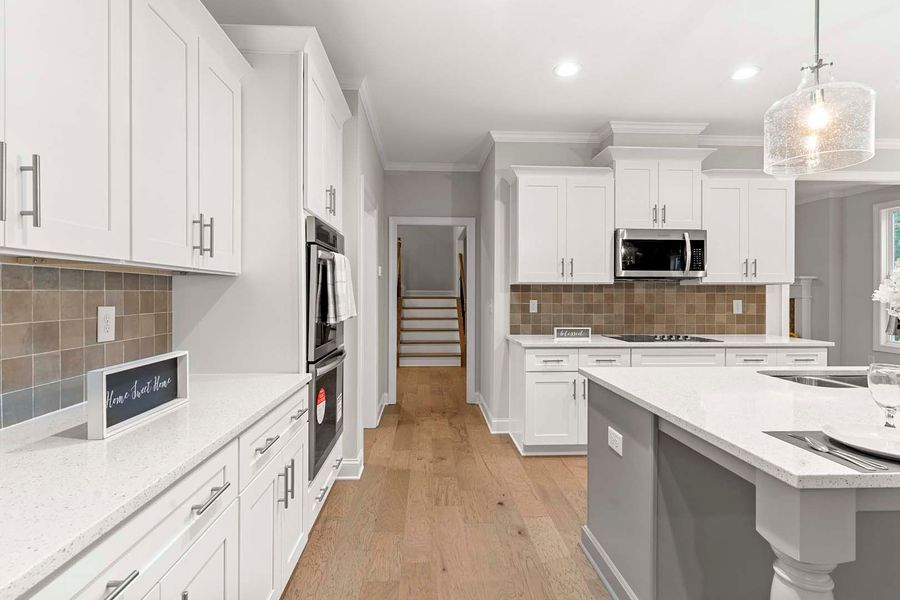 White kitchen with quartz countertops, stainless steel appliances, and wooden floors.