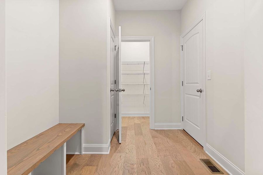 Hallway with light wood floors, white walls, a bench, and pantry.