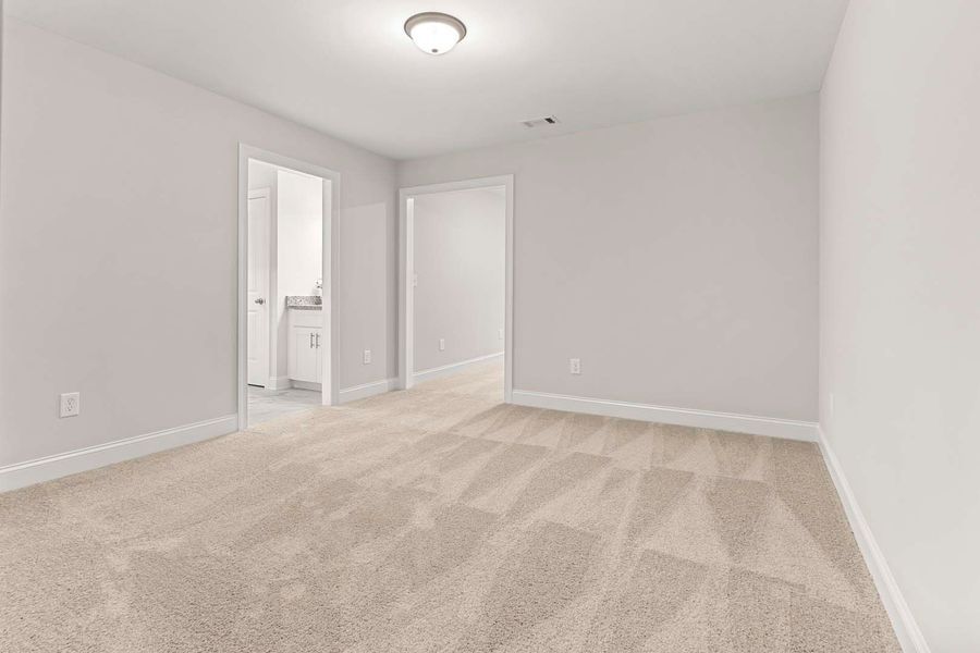 Empty bedroom with light-colored carpet and walls. Two doorways and a ceiling light are visible.
