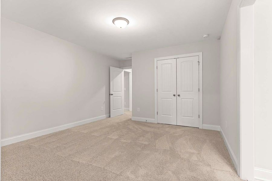 Empty bedroom with light-colored walls, carpet, closet doors, and a doorway to another room.