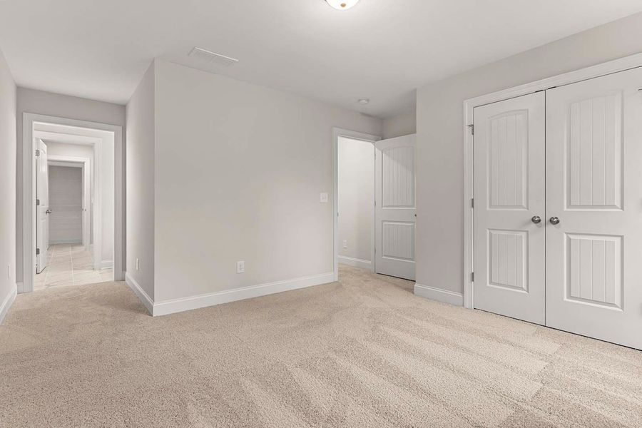 Empty bedroom with beige carpet, white walls, and closed white double doors.