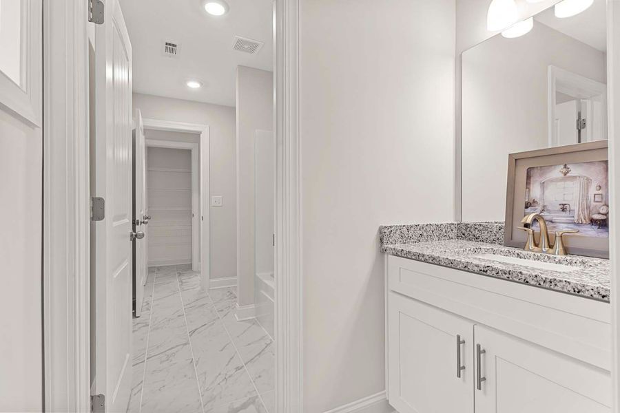 Hallway with white walls and marble flooring, leading to a bathroom with a white vanity and granite countertop.