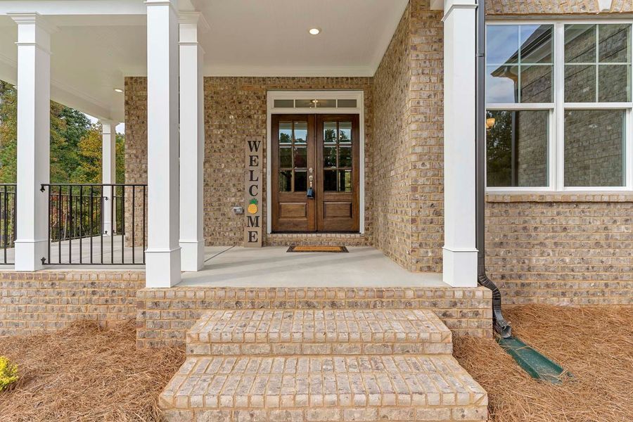 Exterior of a house with brick steps and facade, double wooden doors, and a covered porch.