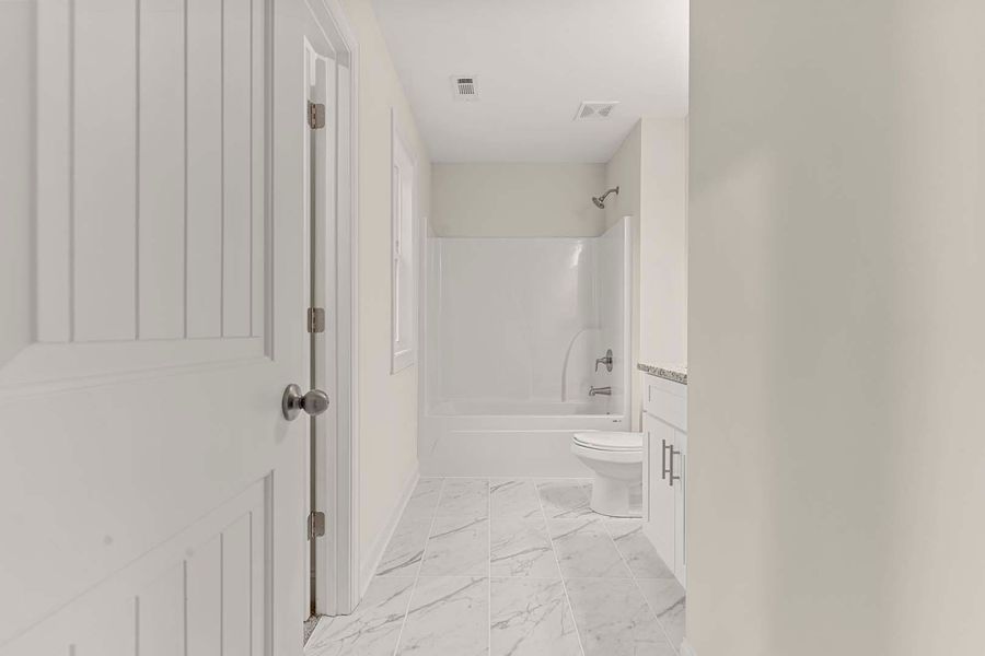 White bathroom with marble floor, shower, toilet, and door.