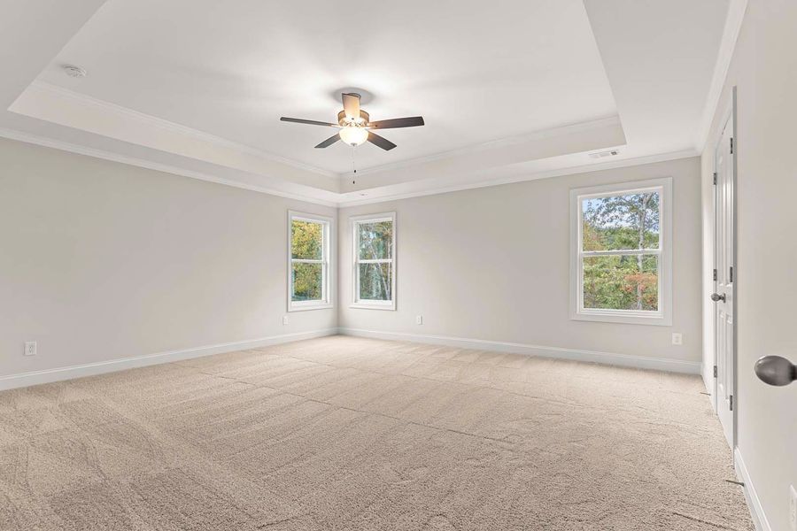 Empty bedroom with neutral colors, carpet, windows, and a ceiling fan.