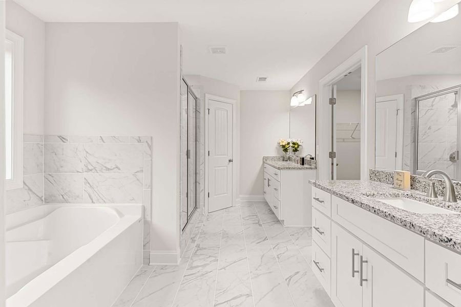 Bright white bathroom with a tub, double vanity, shower, and marble-like tile.