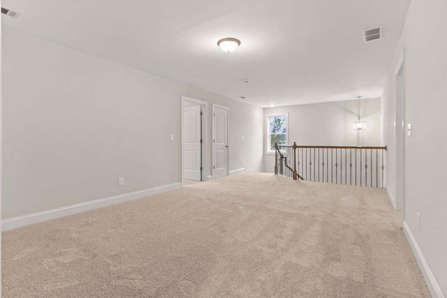 Empty bonus room with beige carpet, white walls, and a staircase.
