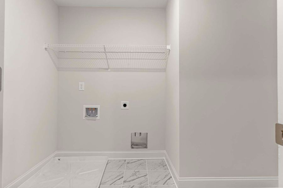 Empty laundry room with gray walls, a wire shelf, and water/dryer hookups.