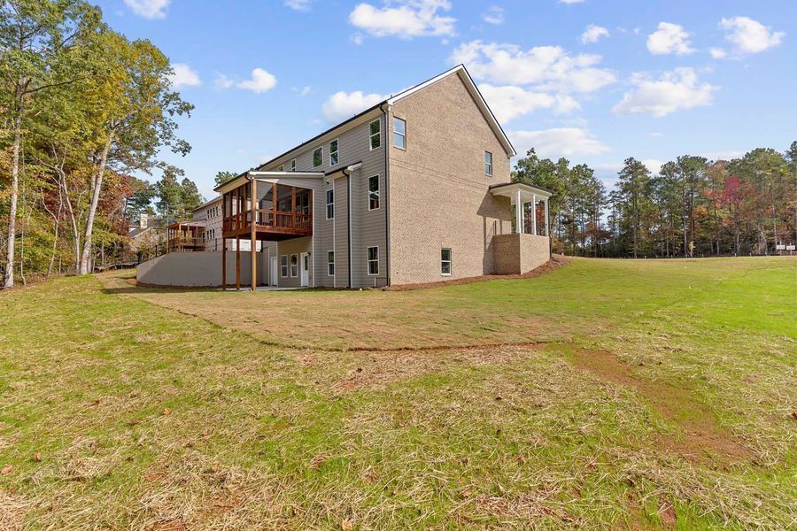 Brick house with porches, on a grassy lot with trees under a blue sky.