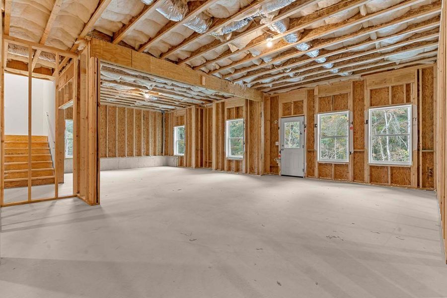 Unfinished interior of a house, exposed wooden framing, concrete floor, windows, and a staircase.