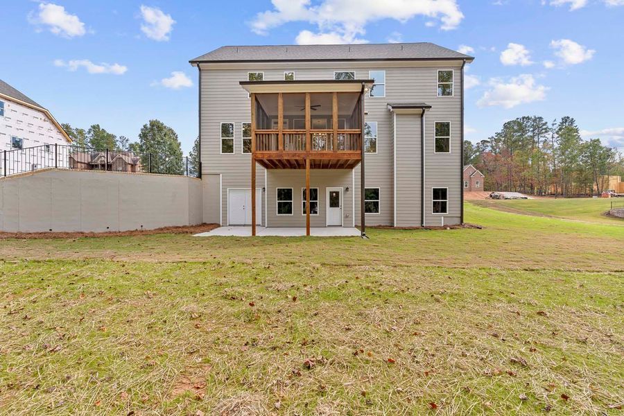 Rear view of a two-story gray house with a screened-in porch, overlooking a grassy backyard.
