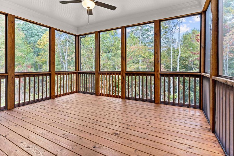 Screened-in porch with wood floor and railings. Large windows reveal a wooded outdoor view.