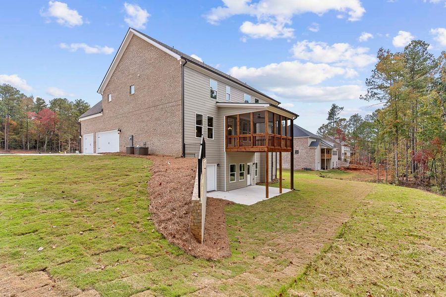 Two-story brick house with a screened porch, built on a hillside with a grassy lawn and woods in the background.