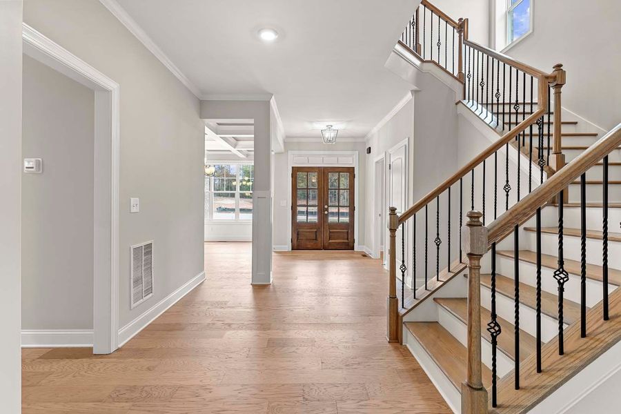 A bright foyer with hardwood floors, stairs, and double wooden doors.