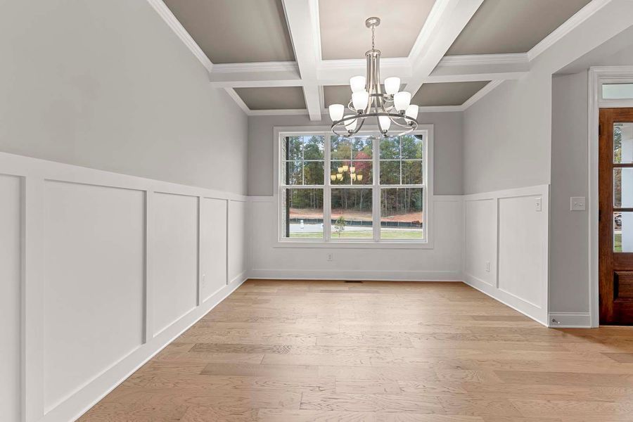 Empty dining room with wood floor, white wainscoting, gray walls, window, and chandelier.