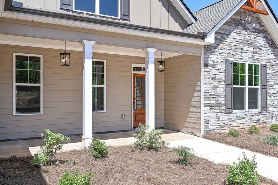 Beige house with stone accents, front porch, windows, and brown door.