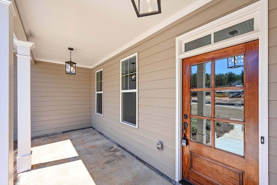 Covered porch with brown door, windows, and tan siding. Two hanging lanterns.