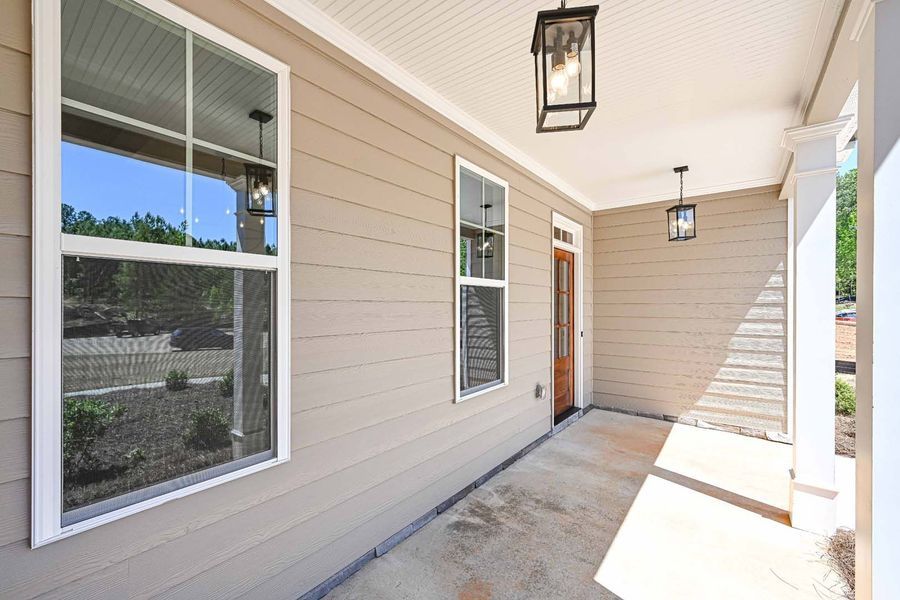 Porch with tan siding, windows, and hanging lights; a wooden door is visible.
