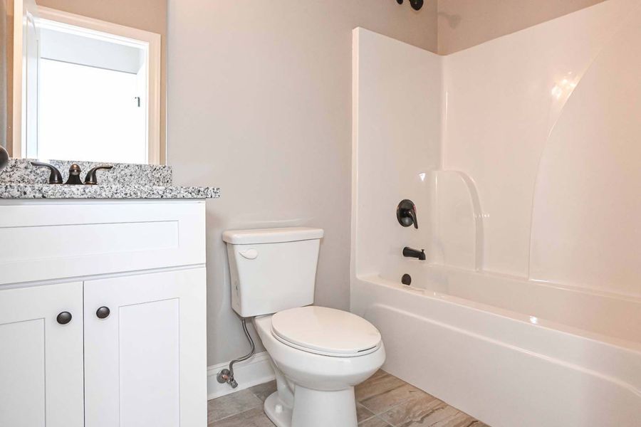 Bathroom with white vanity, toilet, and bathtub; gray walls and flooring.