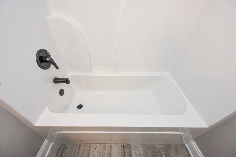 White bathtub and shower surround with black faucet in a bathroom with wood-look flooring.