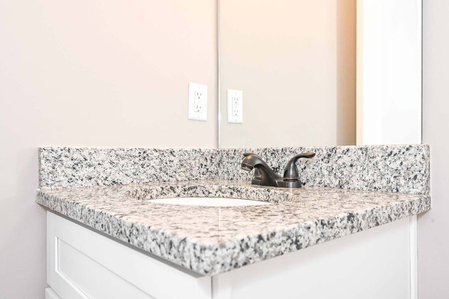 Bathroom vanity with granite countertop and black faucet, with mirror.
