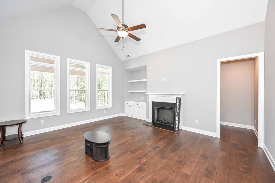 Living room with wood floors, fireplace, built-in shelves, and three windows.