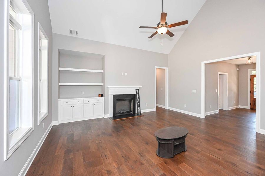 Empty living room with fireplace, built-in shelves, hardwood floors, and a dark coffee table.
