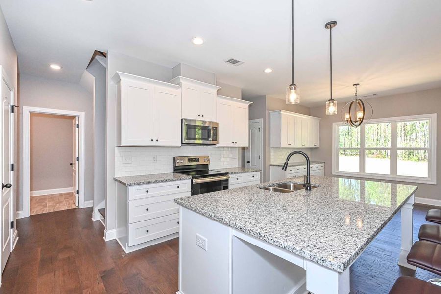 White kitchen with island and stainless steel appliances, dark wood floor, and gray walls.