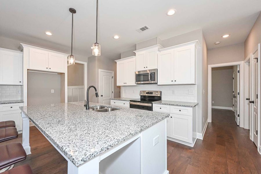 Modern white kitchen with granite island, stainless steel appliances, and dark wood floors.