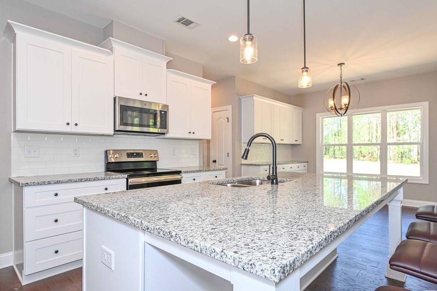 White kitchen with granite countertops, stainless steel appliances, and pendant lights.