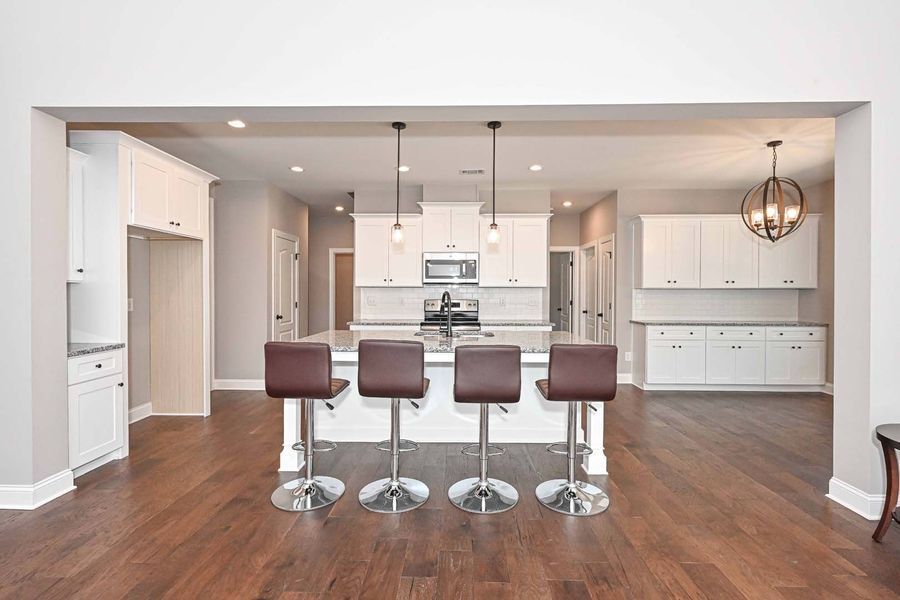 Modern kitchen with white cabinets, island with bar stools, and dark wood floors.