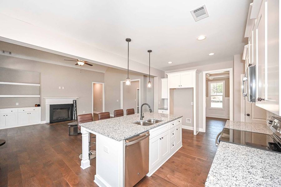 Spacious kitchen with island, stainless steel appliances, and hardwood floors, open to a living area with a fireplace.