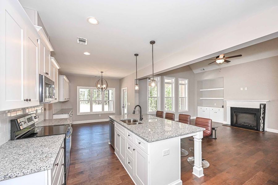 Open-concept kitchen with white cabinets, granite counters, and island, leading to living room with fireplace.
