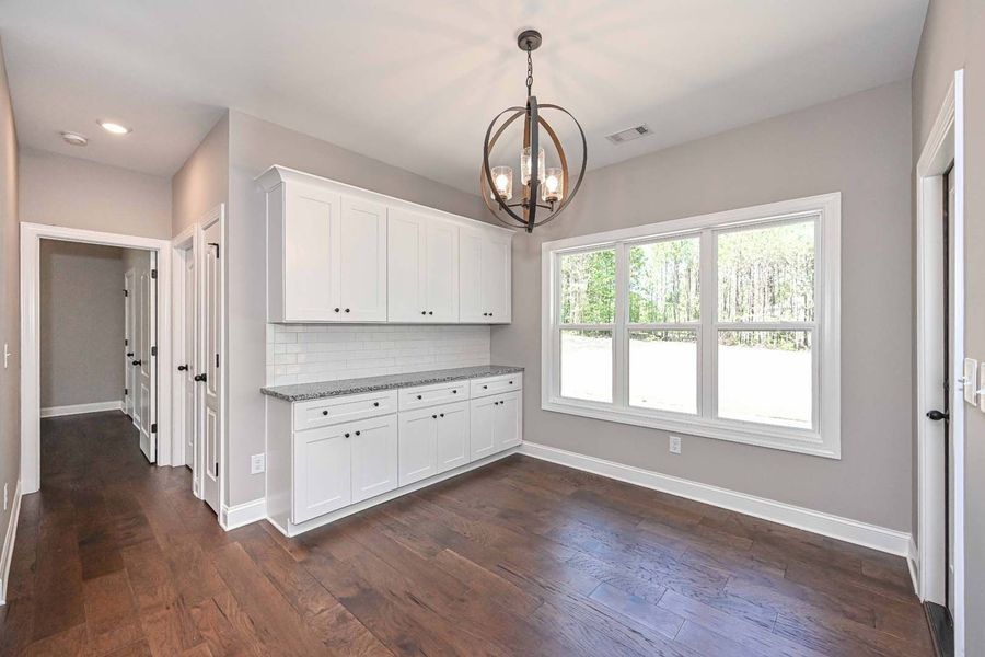 A dining area with white cabinets, dark wood floors, and a large window overlooking greenery.