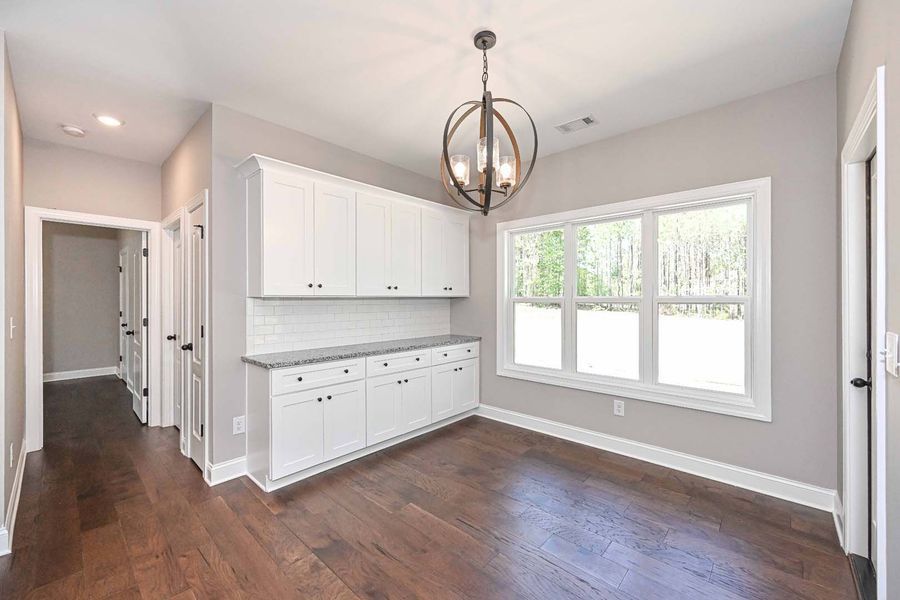 Dining room with white cabinets, large window, dark wood floors, and hanging light fixture.