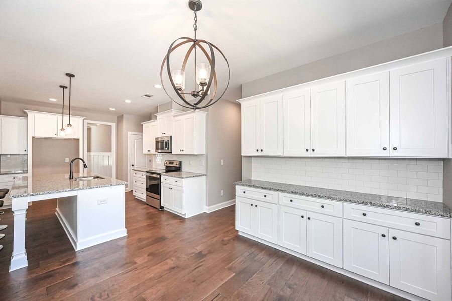 Bright kitchen with white cabinets, granite countertops, and wood flooring.
