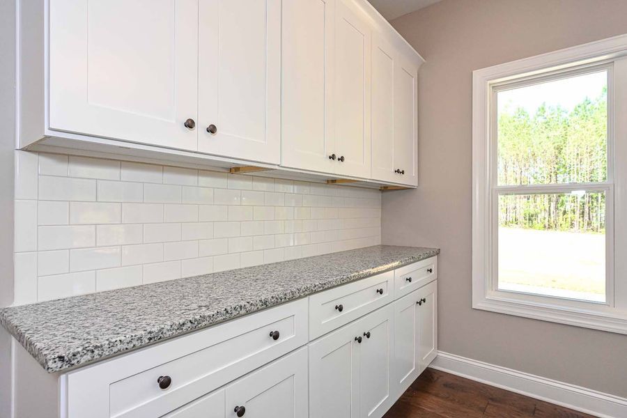 White kitchen pantry with granite countertop, cabinets, and a window overlooking trees.