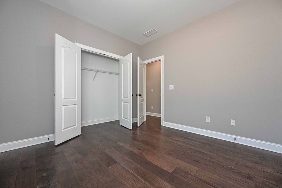 Empty room with gray walls, dark wood floor, white doors, and closet.