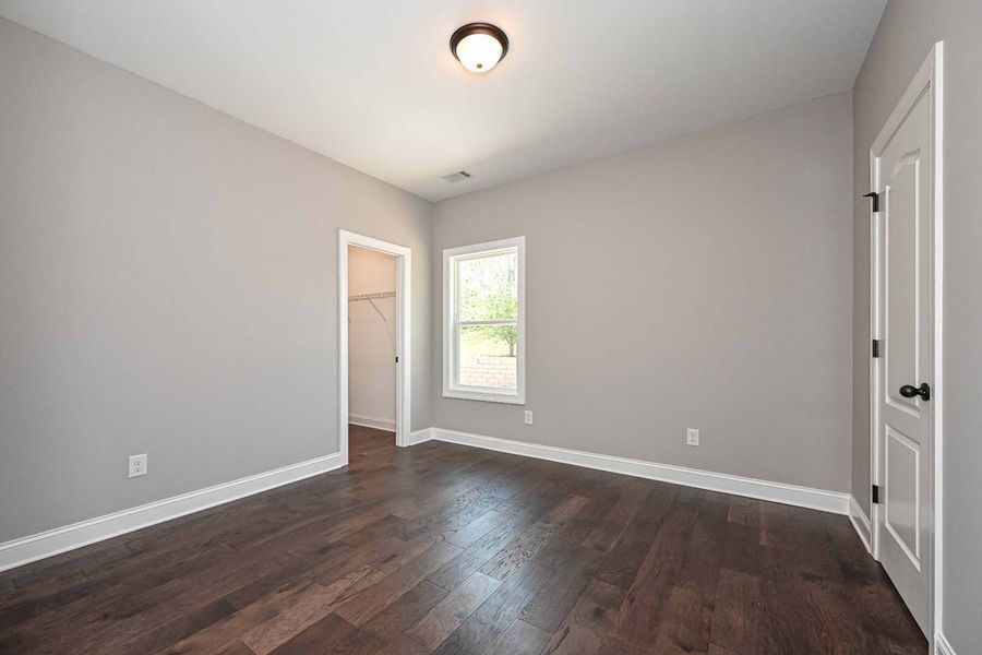 Empty room with gray walls, dark wood floor, white trim and door, a window, and a closet.