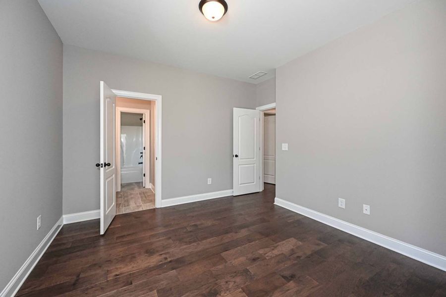 Empty room with gray walls, dark wood floor, and three white doors open.