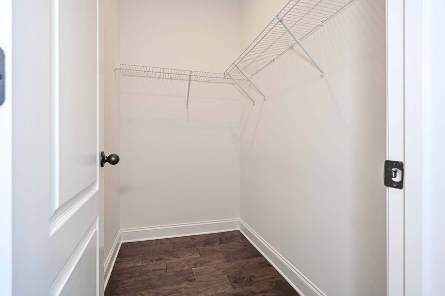 Empty closet with wire shelving, white walls and door, brown floor.