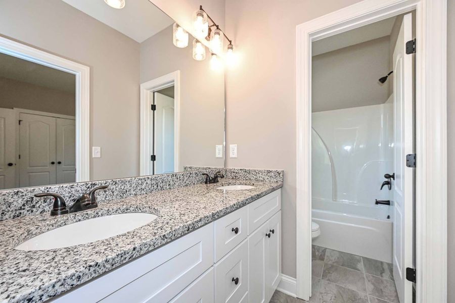 Bathroom with white vanity, granite countertop, large mirror, and doorway to a bathtub.