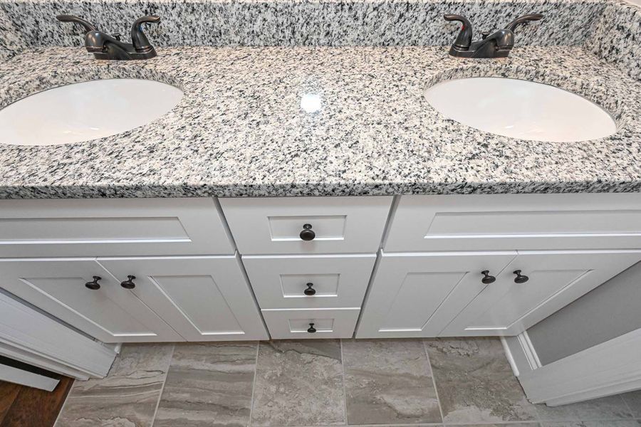 White bathroom vanity with two sinks and granite countertop; brown hardware.