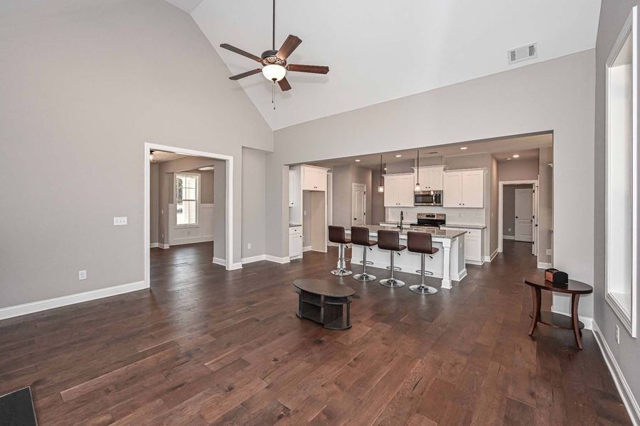 Spacious open-concept living area with hardwood floors, kitchen, and vaulted ceiling; neutral colors, modern style.