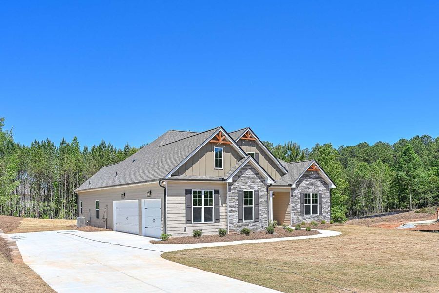 Ranch-style house with stone facade and beige siding, concrete driveway, clear blue sky, and surrounding trees.