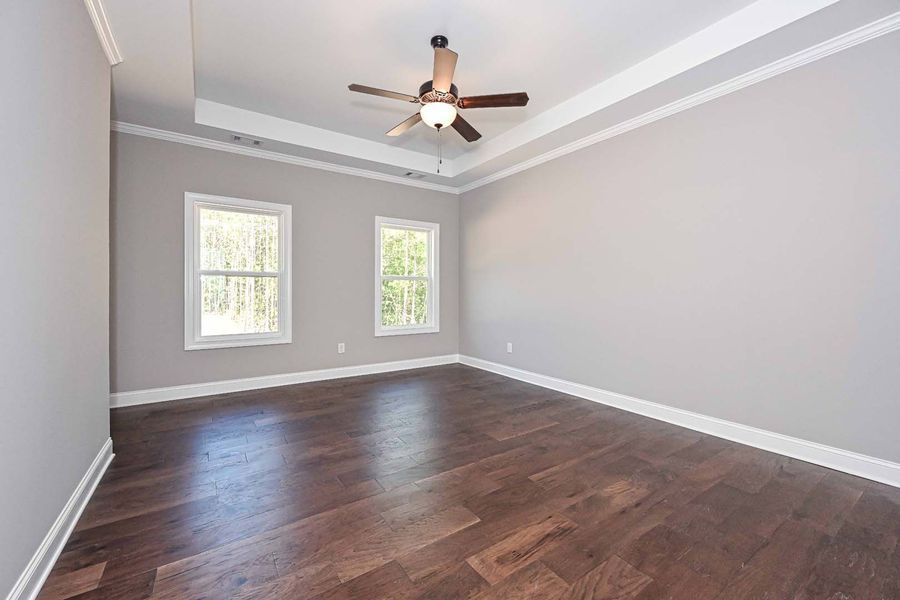 Empty bedroom with gray walls, wood floor, two windows, and a ceiling fan.