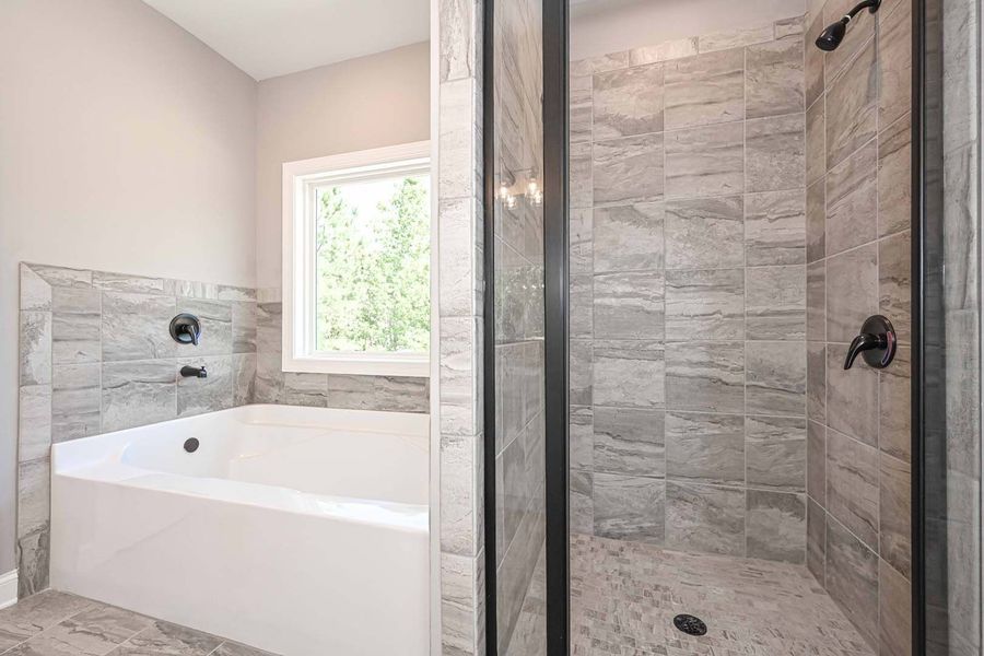 Bathroom with a white tub and gray tiled walls, a shower with a glass door, and a window.