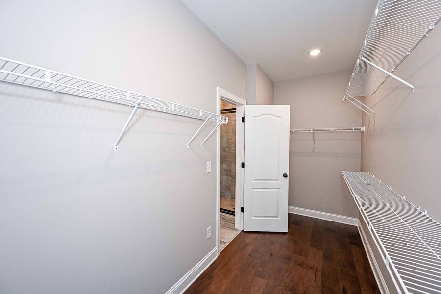 Empty walk-in closet with wire shelving and wooden floor, light gray walls, door to a bathroom.