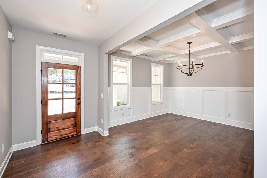 Dining room with coffered ceiling, dark wood floor, white trim, and wood door.